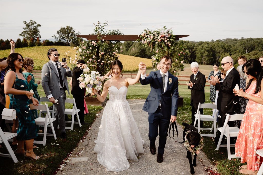 Bride & Groom celebrating wedding ceremony at Yarra Ranges Estate showcasing arbour, aisle décor, and views across the vineyards in the Yarra Valley